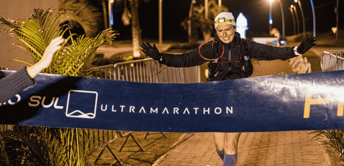 Rachel Belmont crossing finish line at night with Extremo 'Sul Ultramarathon' banner