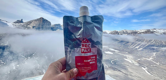 Hand holding a RECPAK complete meal for the backcountry with Baffin Island  mountainous landscape in the background